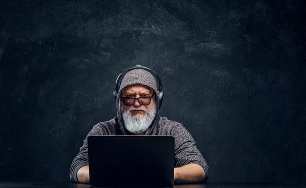 Cool elderly man with headphones typing on laptop - Foto, imagen