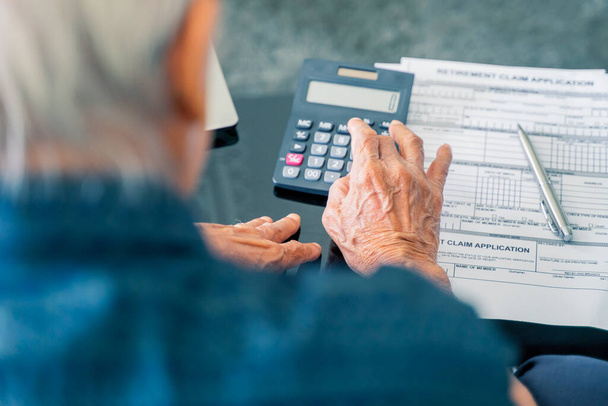 Idős ember kiszámítja megtakarításait nyugdíjazási nyomtatvánnyal az asztalon, miközben otthon ül - Fotó, kép