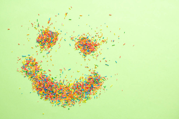 Lachende emoji gemaakt van zoete kleurrijke suiker hagelslag op groene achtergrond met gratis kopieerruimte. - Foto, afbeelding