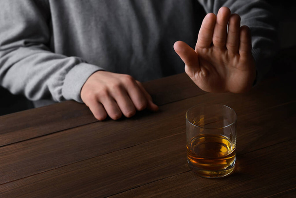 Man refusing to drink whiskey at wooden table, closeup. Alcohol addiction - Zdjęcie, obraz
