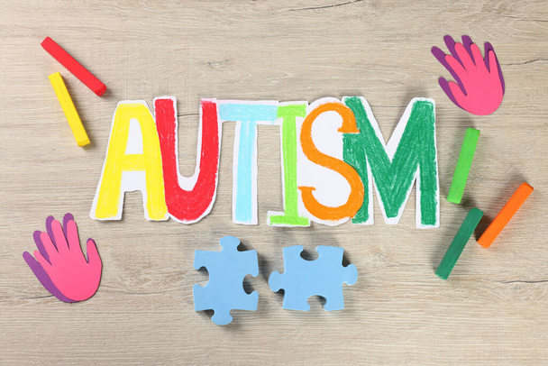 Word Autism made of paper, puzzle pieces and crayons on white wooden table, flat lay - Photo, Image