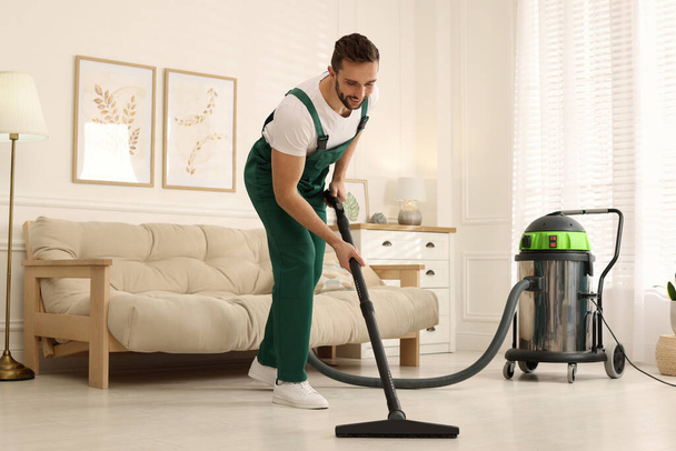 Professional janitor vacuuming floor in living room - Fotó, kép
