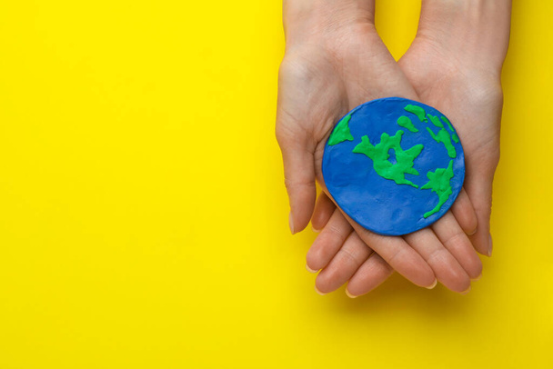 Woman holding plasticine model of planet on yellow background, top view with space for text. Earth Day - Φωτογραφία, εικόνα