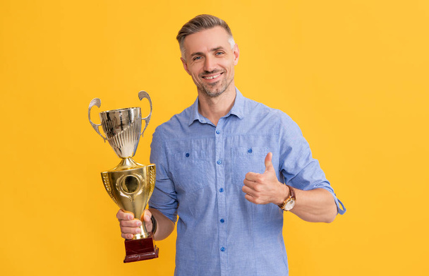 щасливий чоловік тримає золоту чашку і показує великий палець вгору, успіх
 - Фото, зображення