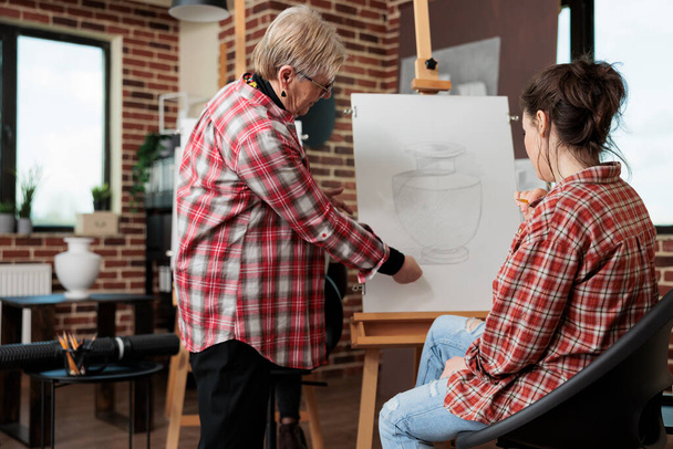 Пожилой учитель рисования показывает технику рисования молодому художнику - Фото, изображение