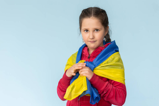 flag of Ukraine in hands of happy girl Ukrainian. child smiles wearing Ukrainian flag blue and yellow flag of Ukraine fluttering on blue sky. - 写真・画像