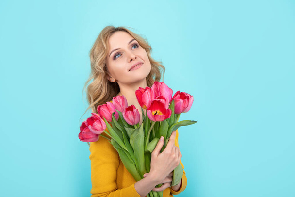 soñadora mujer joven feliz con flores de tulipán de primavera sobre fondo azul - Foto, imagen