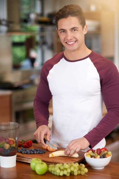 Its tasty and nutritious. Portrait of a happy young man preparing a healthy breakfast of fruit in his kitchen at home. - Photo, image