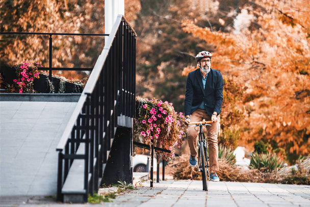 Successful middle-aged businessman riding bicycle on his way to work through the city. - 写真・画像