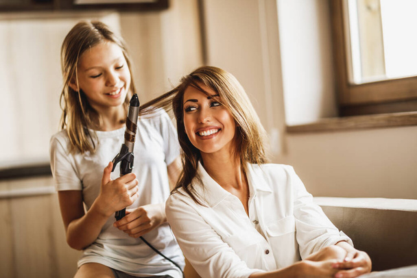 Little daughter is having fun and playing hairdresser with her young mother at home. - Foto, Imagen
