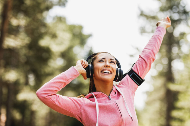 Jonge mooie glimlachende vrouwelijke loper luisteren naar muziek en voor te bereiden op joggen outdoor. - Foto, afbeelding