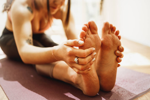 Close up of a relaxed young woman doing stretching exercise while practicing yoga at home. - 写真・画像