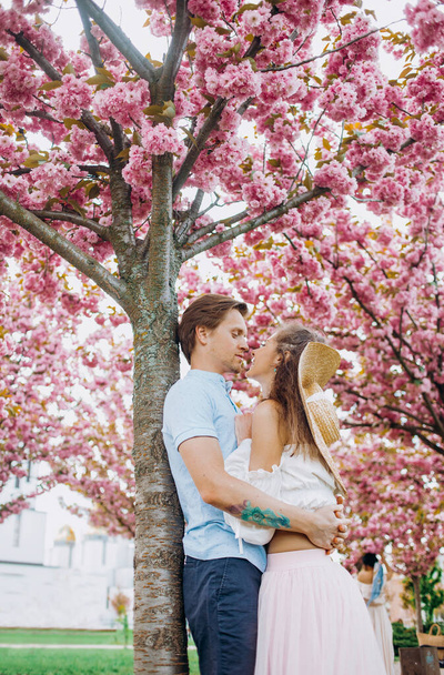 Young couple hugging in the park. Alley with sakura trees - Foto, afbeelding