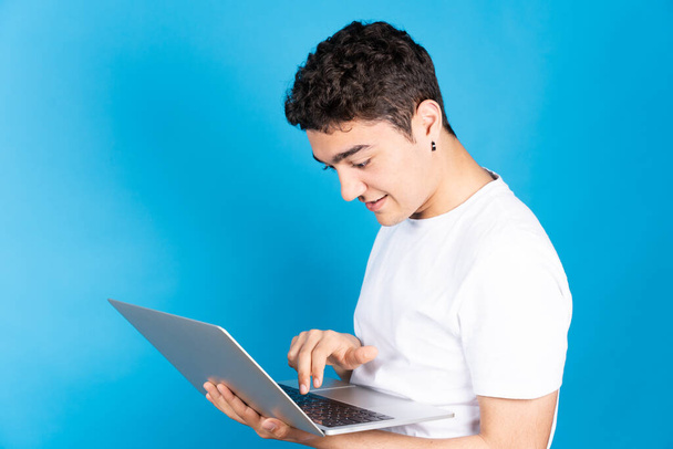 Hispanic young man typing on keyboard of laptop isolated on blue background. - Photo, image