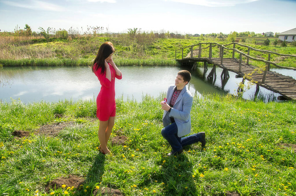 Un hombre en un prado está de rodillas, le da a una chica un anillo y se ofrece a casarse con él.. - Foto, imagen