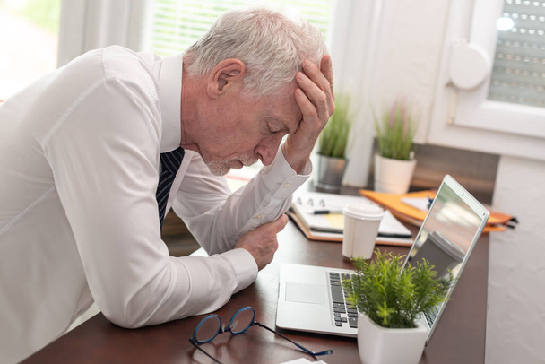 Stressed businessman sitting in office with hand on forehead - Photo, Image