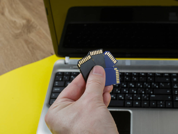 memory card and laptop on a yellow background. hand rezhit memory cards on the background of a laptop. backup concept. - Foto, afbeelding