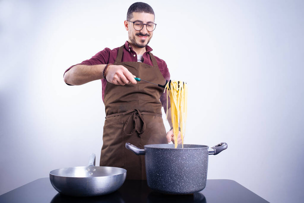 Caucasian white man with apron cooking homemade spaghetti on white background in horizontal shot - Fotó, kép