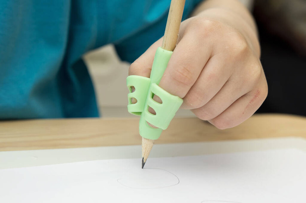 Kid writing with pencil holder. silicone aid grip helps to learn and practice to hold pen in correct position. Correction or rehabilitation of hand writing. - Zdjęcie, obraz