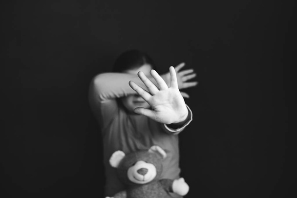 Violencia infantil y concepto de abuso. Niña sentada en una habitación oscura, mostrando señal de stop - Foto, Imagen