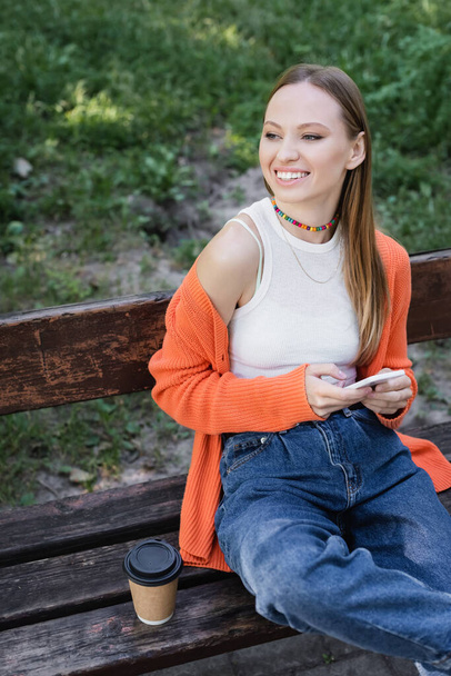 femme heureuse femme tenant smartphone et assis sur le banc - Photo, image