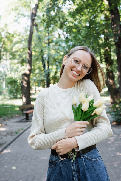 happy woman in glasses holding bouquet of tulips in green park - Foto, Imagen