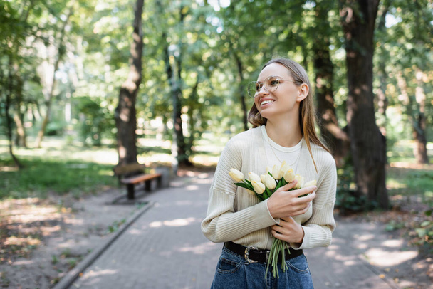 happy woman in glasses holding bouquet of tulips in green park - Foto, Imagem