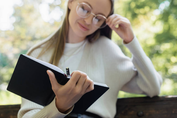 blurred woman in glasses holding notebook and pen - Foto, Imagen