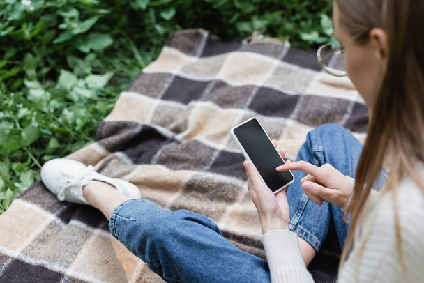 high angle view of woman in glasses using smartphone with blank screen while sitting on checkered plaid - Foto, Imagem