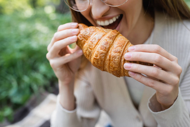 vista ritagliata di donna felice che tiene croissant mordente  - Foto, immagini