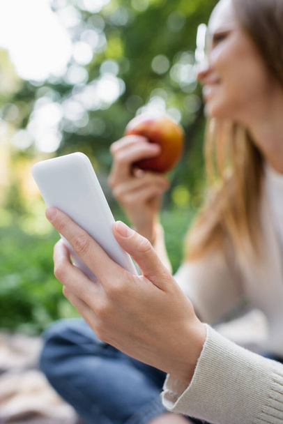 blurred woman holding apple and smartphone in hands - Foto, afbeelding
