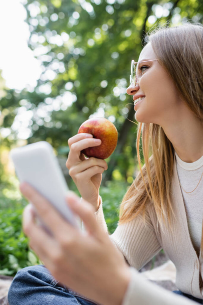 happy woman in glasses holding apple and smartphone in hands - Фото, изображение