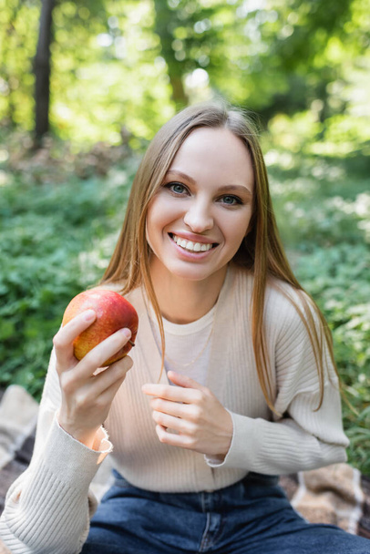 happy woman holding red tasty apple in green park - Фото, изображение