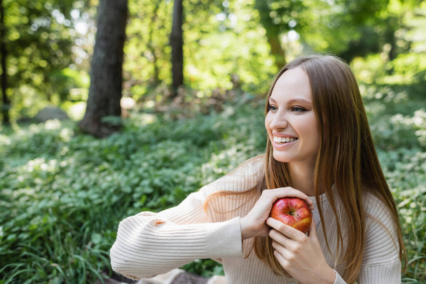 cheerful woman holding red tasty apple in green park - 写真・画像