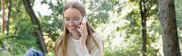onnellinen nainen lasit ottaa puhelun älypuhelimeen vihreässä puistossa, banneri - Valokuva, kuva