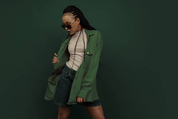 Monochrome portrait of female fashion model in shorts and shirt isolated on dark green background. Concept of beauty, art, fashion, youth and emotions - Φωτογραφία, εικόνα