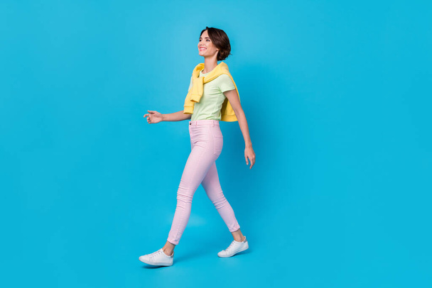 Full size photo of pretty young brunette lady go wear t-shirt pants shoes isolated on blue background - 写真・画像