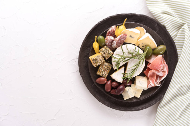 Charcuterie tábla választéka sajtok, szalámi és prosciutto szolgált olívabogyó fekete tányéron fehér asztal háttér. Olasz hagyományos tészta, felülnézet - Fotó, kép