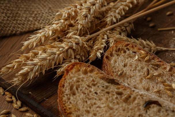 Close-up of homemade bread. Peasant loaf bread and wheat spikelet with space for text. Homemade baking. Gray whole bread on wooden board - Foto, afbeelding