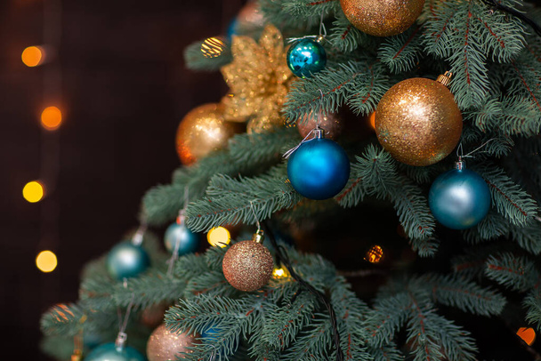 Closeup of Festively Decorated Outdoor Christmas tree with blue and golden balls on blurred sparkling fairy background. Defocused garland lights, Bokeh effect. - 写真・画像