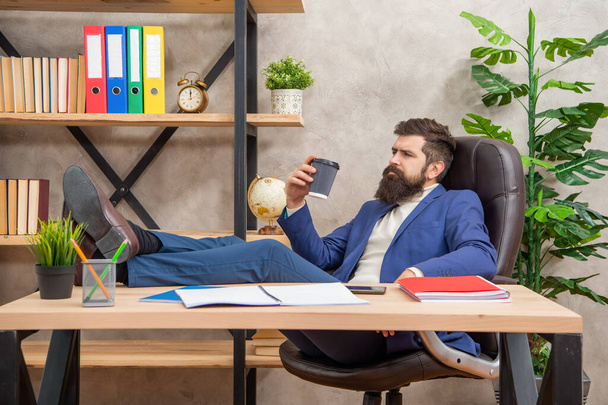 Tired man in suit relaxing with legs on desk during coffee break in office, relaxation - 写真・画像