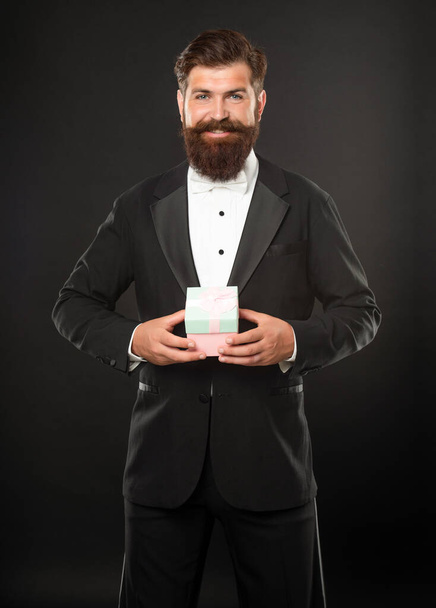 smiling man in tuxedo bow tie formalwear on black background with gift box. boxing day - 写真・画像
