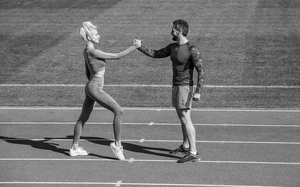 sport man and woman fitness partners celebrate team win with gesture of shake hand after exercising or compete in armwrestling on stadium running track arena outdoor, sport success - Photo, image