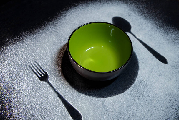 Ceramic green bowl with fork and spoon on table. Fork and Spoon silhouette on white flour. Rustic contrasting background.Food background.  - Φωτογραφία, εικόνα
