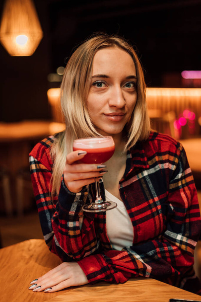 A young beautiful blonde holds a glass with a cocktail in a restaurant - Φωτογραφία, εικόνα