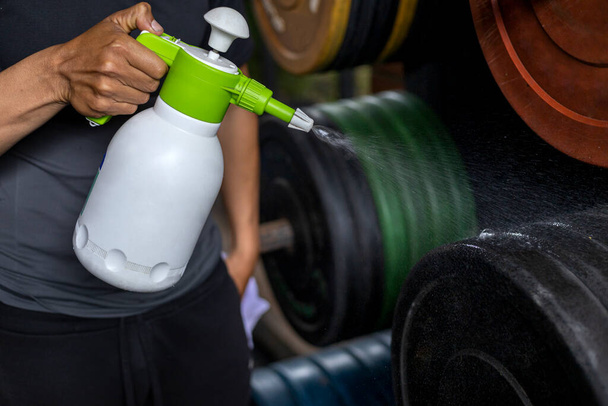 Close-up of a man's hands using a bottle of disinfectant to clean weight discs in the gym. Concept disinfection, cleaning, anti-bacterial - 写真・画像