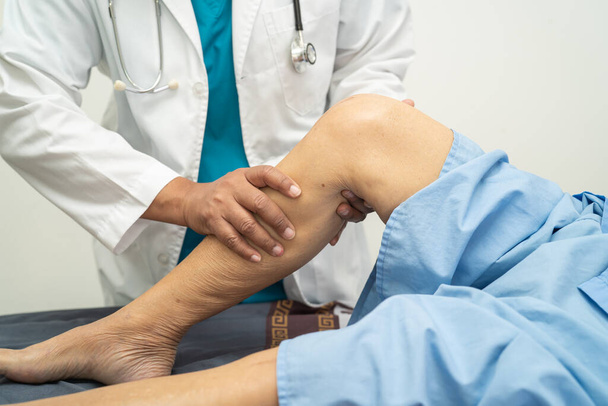 Aziatische arts fysiotherapeut onderzoeken, masseren en behandeling knie en been van senior patiënt in orthopeed medische kliniek verpleegkundige ziekenhuis. - Foto, afbeelding
