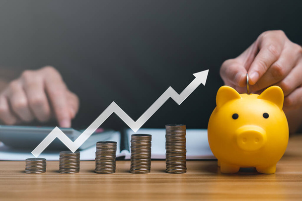 Businessman holding a coin in a piggy bank with graphs and arrows showing charts on his desk. concept of money growth and business finance, successful investment strategy - Photo, Image