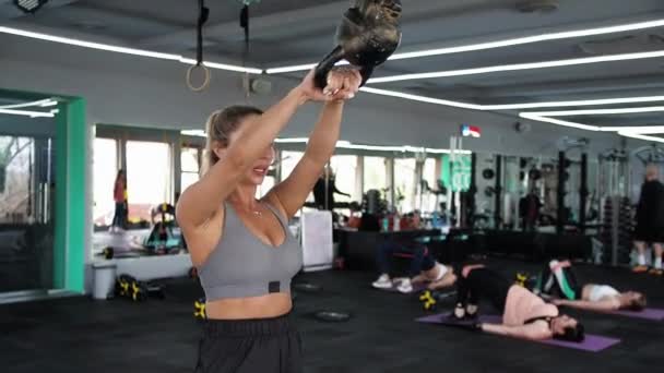 CrossFit Μια ξανθιά γυναίκα προπονείται με μια κέτλμπελ τεντώνει τους μυς. Αθλητικά παιχνίδια - Πλάνα, βίντεο