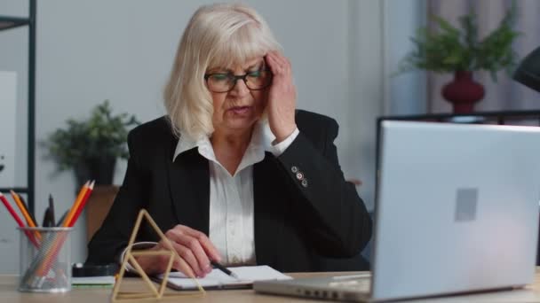 Migain baş ağrısından muzdarip dizüstü bilgisayar kullanan yaşlı kadın ofis çalışanı serbest öğretmen. - Video, Çekim